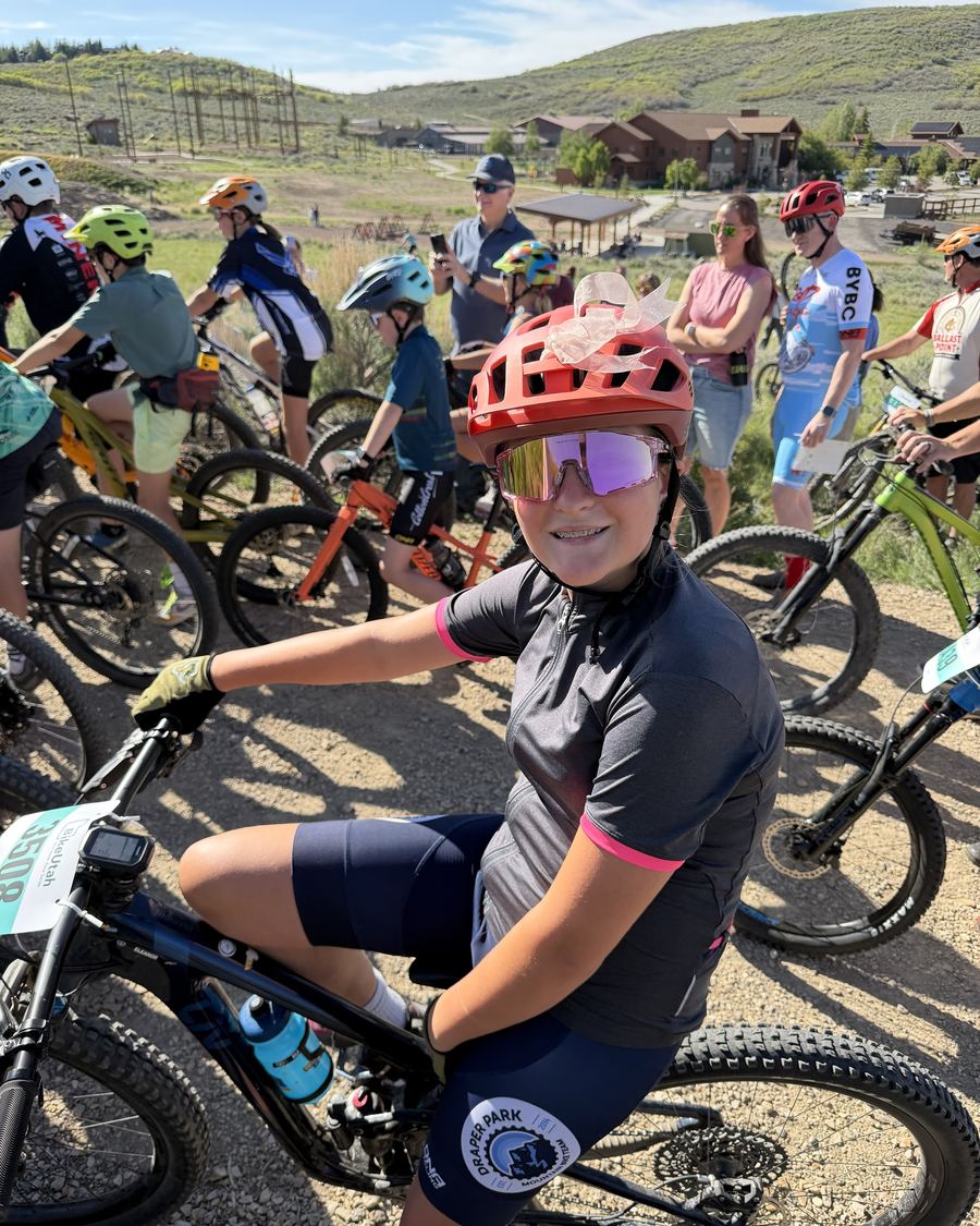 Smiling young rider in a red helmet and pink sunglasses at a race start