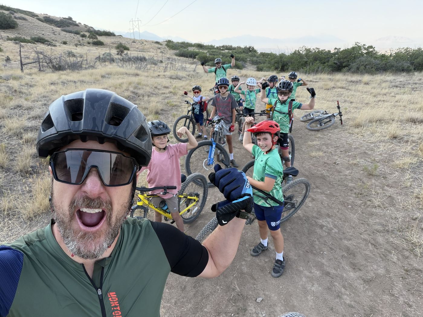 Coach taking a selfie with a group of young riders flexing on a hillside trail