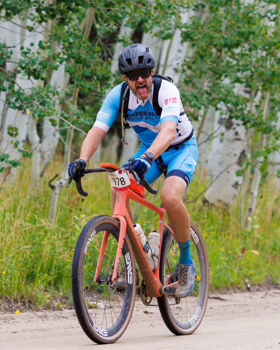 Gravel racer on a muddy carbon bike riding past aspens
