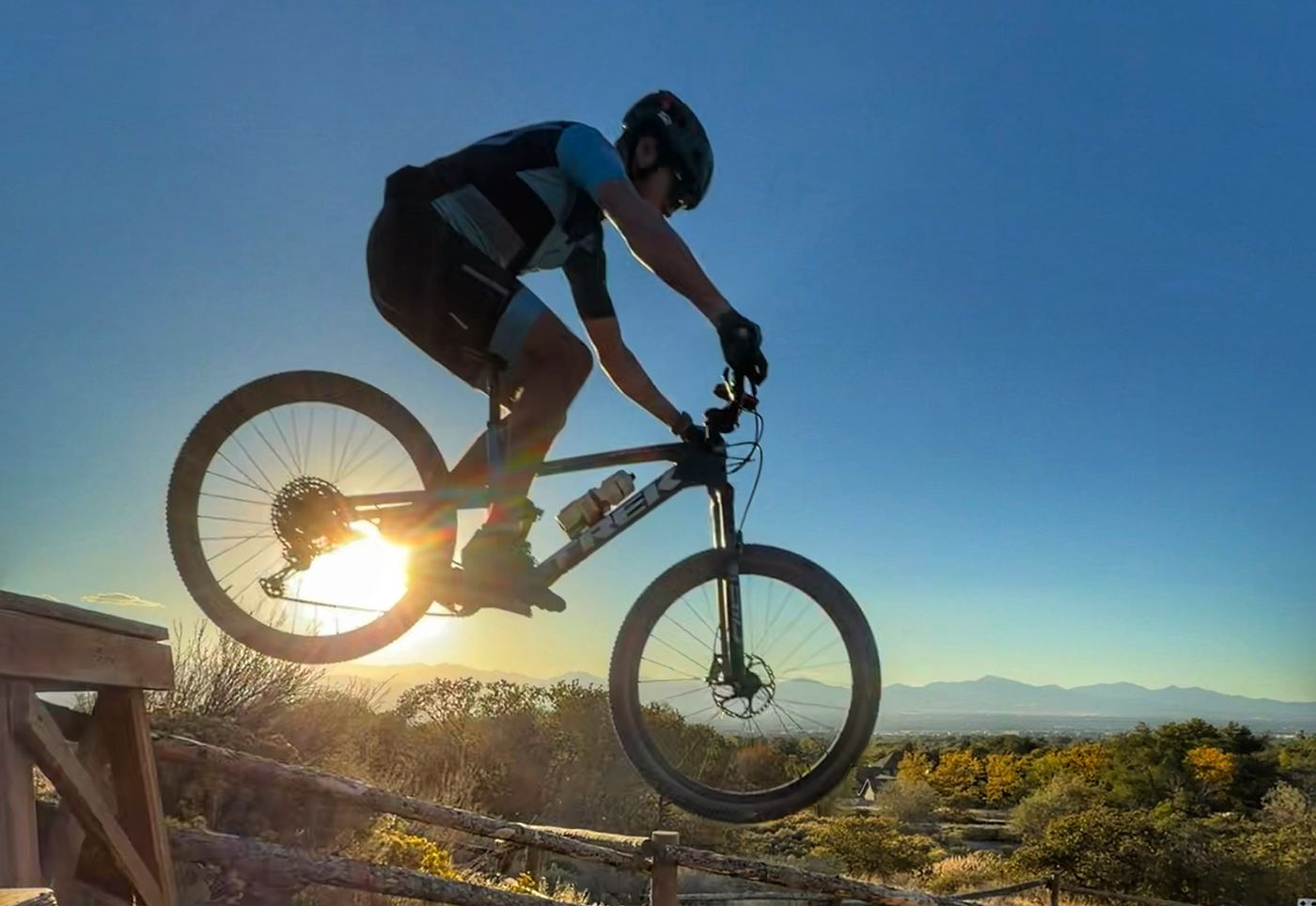 Rider airborne off a wooden drop at sunset above the Salt Lake Valley