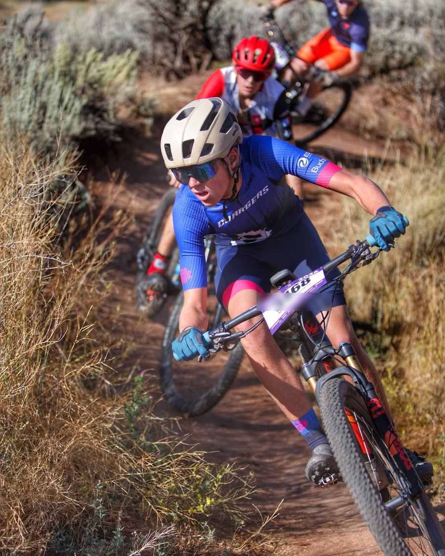 High school racer leading two riders through a sagebrush singletrack corner